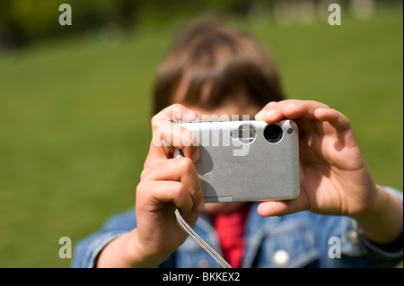 A sette anni di vecchio ragazzo scatta una foto con un piccolo argento fotocamera digitale in un parco, London REGNO UNITO Foto Stock