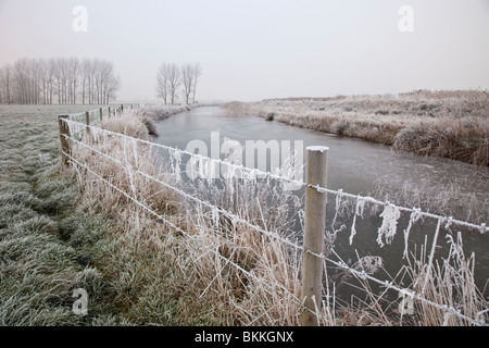 Un fiume congelato accanto a un recinto di filo su un gelido mattino Foto Stock
