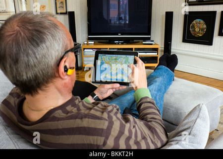 Un uomo seduto nel suo divano, utilizzando un Apple iPad per guardare att il Google-powered app Mappe. Foto Stock