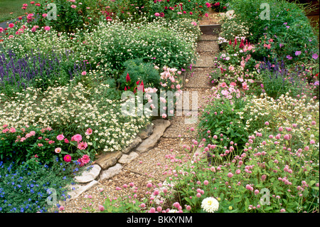 Garden Cottage con percorso fatto di pietre per pavimentazione e roccia cava creando una passerella stabile attraverso un variopinto giardino fiorito Foto Stock