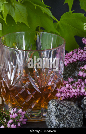 Un bicchiere di whisky sulle rocce con heather e foglie Foto Stock