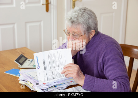 Preoccupato senior donna pensionato titolare di pensione o di rendita con una grande pila di fatture con la mano sopra la sua bocca cercando indignato per un grande Barclaycard carta di credito bill. Regno Unito Foto Stock