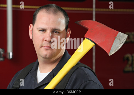 Mid-adulto pompiere holding fire ax in piedi nella parte anteriore del motore fire closeup con sguardo serio sulla faccia Foto Stock