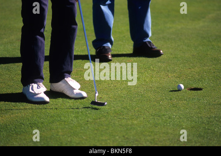 Due amanti del golf putting pallina da golf nel foro su un campo da golf. Foto Stock