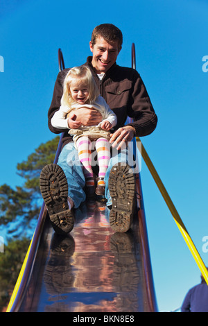 Un padre andando verso il basso della slitta con la sua giovane figlia Foto Stock