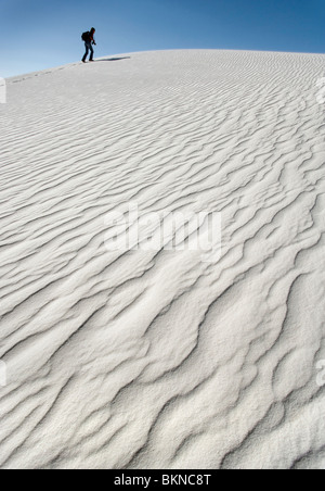 Una persona che cammina fino a bianco grande duna di sabbia a White Sands National Monument, Nuovo Messico. Foto Stock