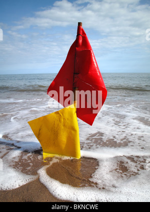 Lavate il rosso e il giallo pesca / aragosta bandiere marker posizionati sulla spiaggia come la marea arriva a. Foto Stock