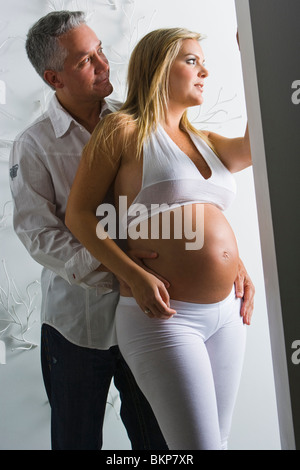 Bionda donna incinta bianco da indossare in piedi con l'uomo dietro di lei Foto Stock