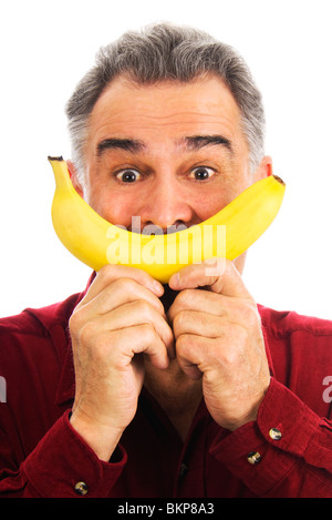 Uomo maturo, indossando una maglietta rossa, detiene una banana giallo con due mani per il suo volto, che rappresenta un sorriso. Foto Stock