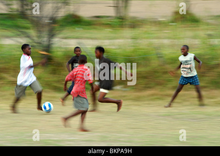 I bambini africani che giocano a calcio a piedi nudi in un campo di Hout Bay a Cape Town, Sud Africa. Foto Stock