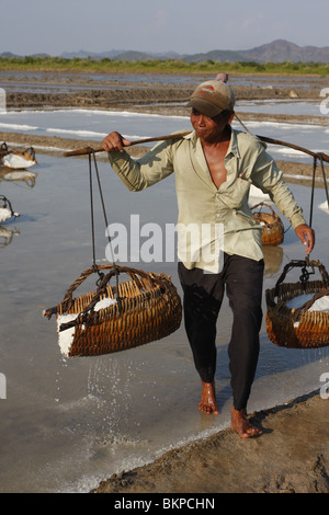 Un uomo porta un pesante carico di sale su un sale agriturismo vicino a Kampot, Cambogia Foto Stock