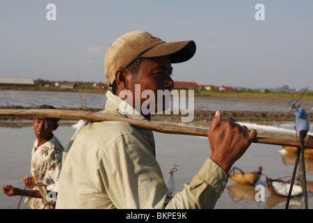 Un uomo porta un pesante carico di sale su un sale agriturismo vicino a Kampot, Cambogia Foto Stock