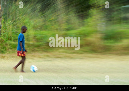 Bambino africano che giocano a calcio a piedi nudi in un campo di Hout Bay a Cape Town, Sud Africa. Foto Stock