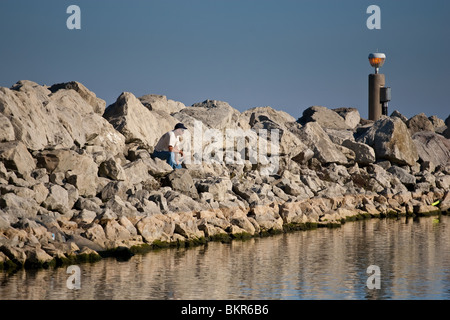 Un pescatore solitario su un breakwall attesa per la sua cattura a mordere, Lago Ontario, Ontario, Canada Foto Stock