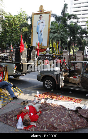 Una maglietta rossa dimostrante la campagna contro il governo è caduto addormentato davanti ad un'immagine della Thailandia del re. Foto Stock