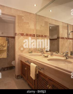 Moderno di colore beige bagno rivestito di piastrelle bagno con grande specchio montato sopra l'unità vanity con sotto-insieme di bacini Foto Stock