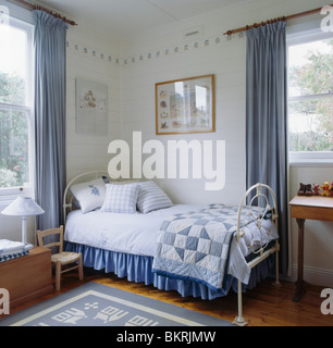 Blue patchwork trapunta e biancheria di colore bianco su bianco in ferro battuto letto in stile vittoriano in blu+a tema bianco Camera bambino con tende blu Foto Stock