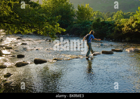 Walker attraversando il fiume Esk su pietre miliari, Eskdale nel Lake District inglese Foto Stock