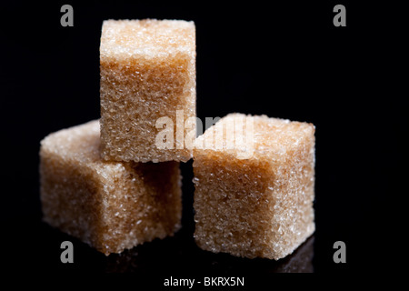 Tre di zucchero di canna i cubi su un Riflettente superficie nera Foto Stock