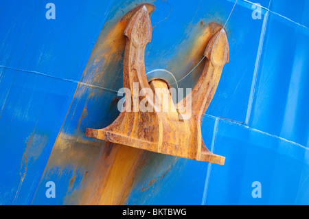 Un arrugginito ancora fornisce il contrasto contro uno scafo blu su un oceano navi. Foto Stock