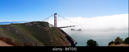 Golden Gate Bridge a Fog San Francisco California | SAN FRANCISCO, California, Stati Uniti - Una nave portacontainer passa sotto il Golden Gate Bridge mentre una fitta nebbia scorre attraverso lo stretto sotto i cieli limpidi. Completato nel 1937, il ponte sospeso si estende per 1,7 miglia (2,7 km) attraverso il Golden Gate, lo stretto che collega la Baia di San Francisco all'Oceano Pacifico. Foto Stock