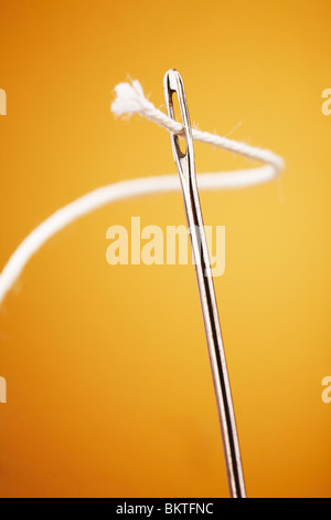 Filo bianco andando attraverso ago closeup su sfondo giallo Foto Stock