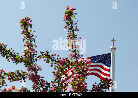 La chiesa cattolica con una croce e una bandiera americana su un palo con un albero in fiore contro il cielo blu angolo basso nessuno orizzontale in Ohio Stati Uniti h-res Foto Stock