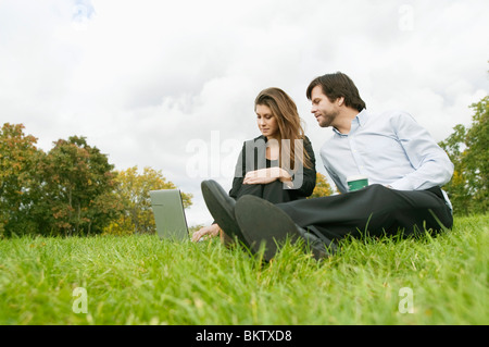 Donna e uomo seduto su un prato con il computer Foto Stock