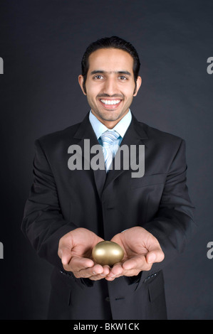 Imprenditore azienda golden egg in mano a tazza, sorridente, ritratto Foto Stock