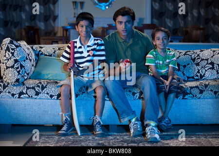 Padre con due figli a guardare i programmi sportivi in televisione Foto Stock