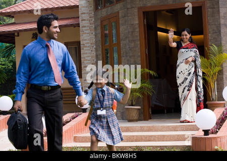 Schoolgirl (8-9) con padre sventolando off a madre, sorridente Foto Stock