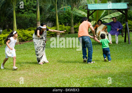 Famiglia giocando "cieco mans bluff' nel giardino, nonni in seduta lo swing Foto Stock