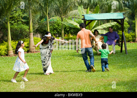 Famiglia giocando "cieco mans bluff' nel giardino, nonni in seduta lo swing Foto Stock