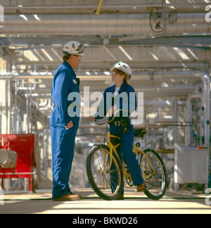 Maschile e Femminile co-lavoratori presso una raffineria di petrolio nel Delaware, Stati Uniti d'America. Le biciclette sono utilizzati per aggirare il grande impianto. Foto Stock