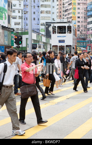 Le persone che attraversano la strada nella parte anteriore del tram in Hong Kong Foto Stock