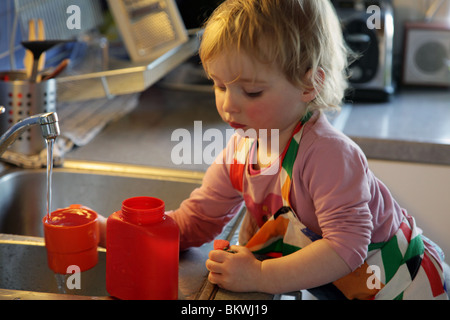 MADRE DI DUE ANNI: Bimba di due anni gioca giocando con il lavandino d'acqua cucina casalinga modello rilasciato Foto Stock