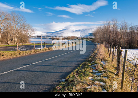 Un solitario strada conduce attraverso il ghiaccio coperto Poulaphouca serbatoio e sul verso la Contea di Wicklow Mountains. Foto Stock