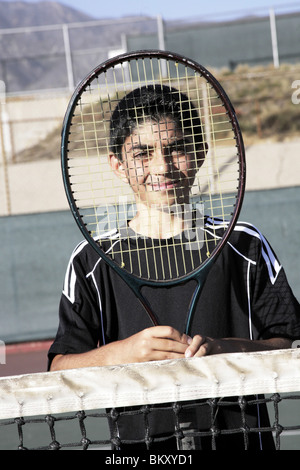 Ragazzo che guarda attraverso le corde di una racchetta da tennis Foto Stock