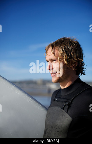 Giovane maschio surfer a Pacific Beach in San Diego California in una giornata di sole guardando lontano dalla telecamera, osservando l'oceano. Foto Stock