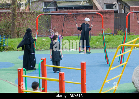 I musulmani compresi una donna in un burkha in un parco giochi in una zona musulmana di Blackburn Lancashire, Regno Unito. Foto Stock