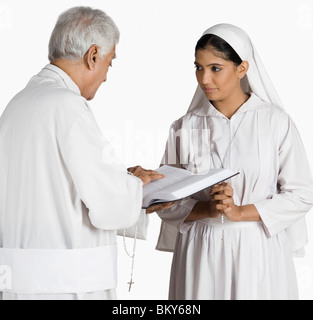 Sacerdote della lettura della Bibbia con una monaca in piedi di fronte a lui Foto Stock