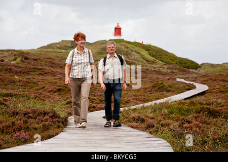Giovane camminando lungo il percorso di legno attraverso le dune, il faro in background, Amrum island, Schleswig-Holstein, Germania Foto Stock