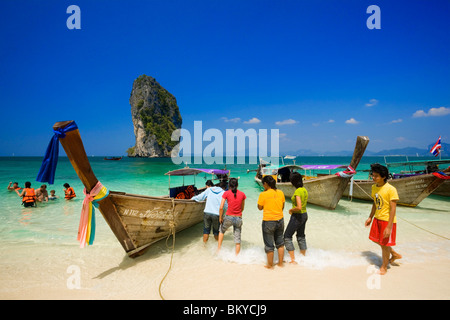 Barche ancorate alla spiaggia, i turisti con i giubbotti di salvataggio in piedi in acqua, Ko Poda in background, Laem Phra Nang, Railay, Krabi, tailandese Foto Stock