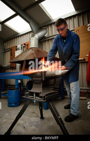 La formazione di scintille volare il metallo caldo come un giovane uomo impara fabbro di base delle competenze a Ceredigion formazione professionale centro, REGNO UNITO Foto Stock