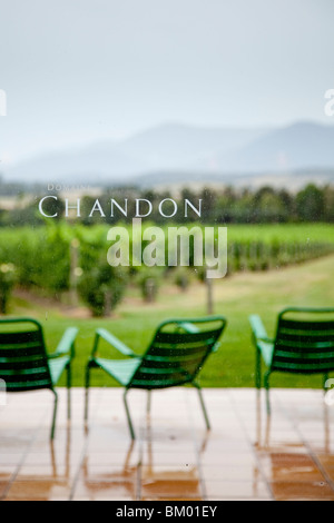 Domaine Chandon cantina con sedie verde di pioggia patio con vista sul vigneto, boccole, alberi e colline in background. Foto Stock