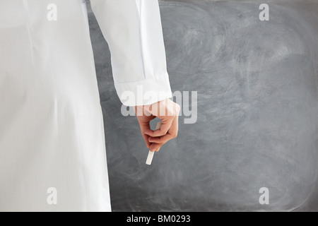 Vista posteriore del docente femminile in abiti da laboratorio azienda chalk contro la lavagna vuota. Spazio di copia Foto Stock