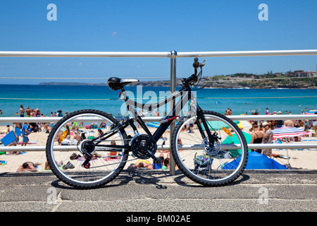 Una bicicletta appoggiata contro una ringhiera sul lungomare a Bondi Beach Sydney con lucertole da mare sulla sabbia in background Foto Stock