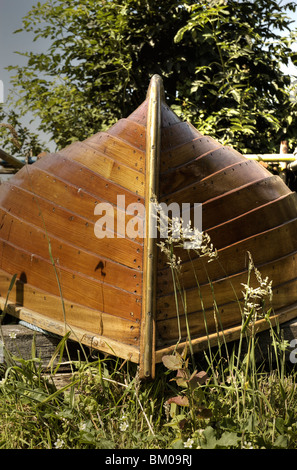 Un di legno barca a remi capovolto su una riva di un fiume Foto Stock