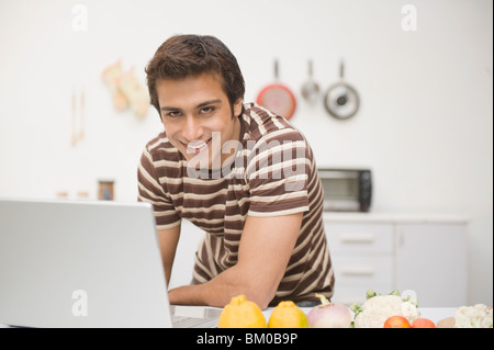 Uomo che utilizza un computer portatile su un bancone cucina con verdure Foto Stock