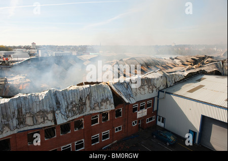 Grande fabbrica e magazzino collassato e a covare dopo un grave incendio notte prima - Vigili del Fuoco basso smorzamento Foto Stock